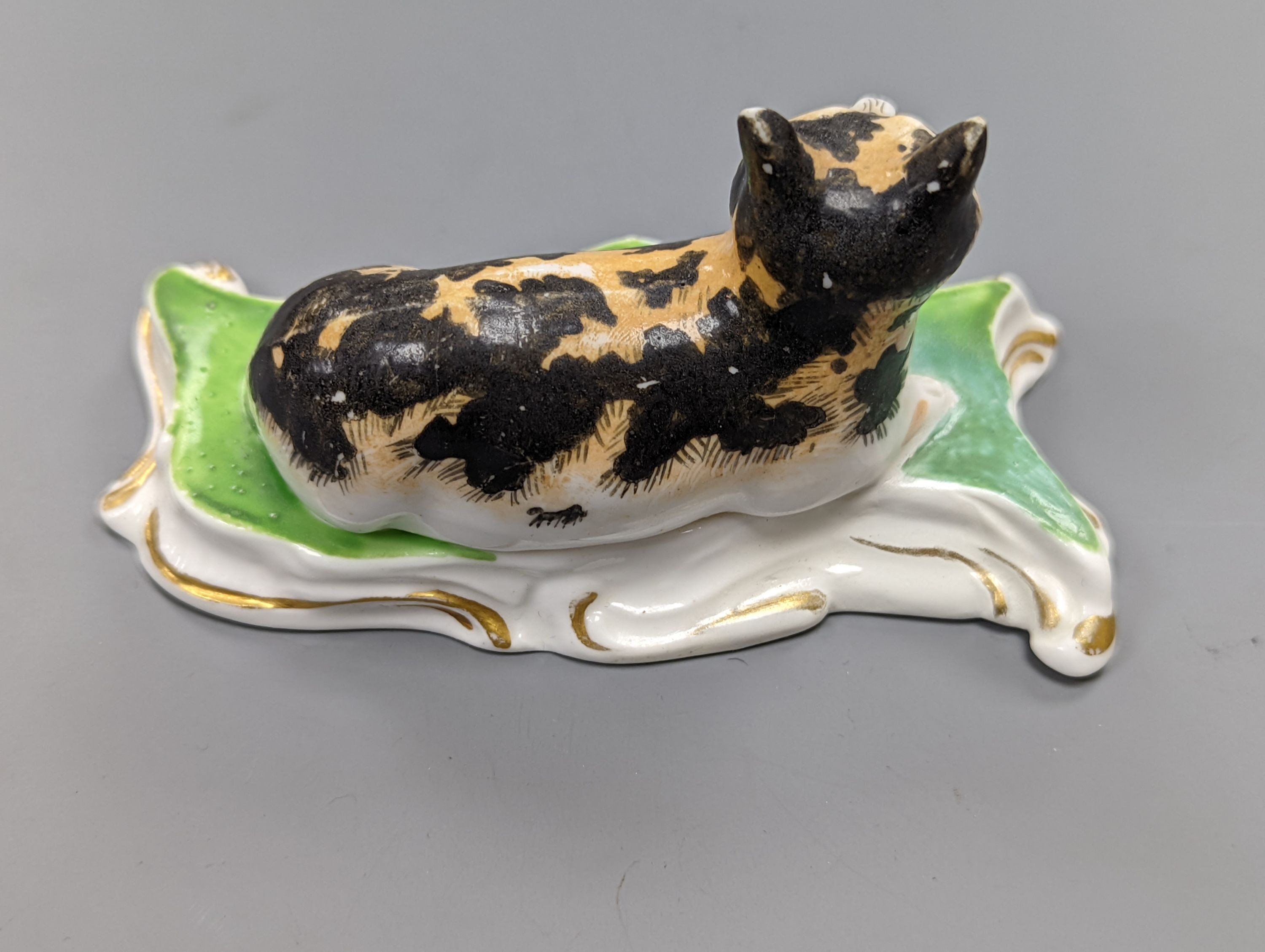 A rare Staffordshire porcelain figure of a recumbent tabby cat, c.1830-50, on a scroll work base, 11.5 cm long